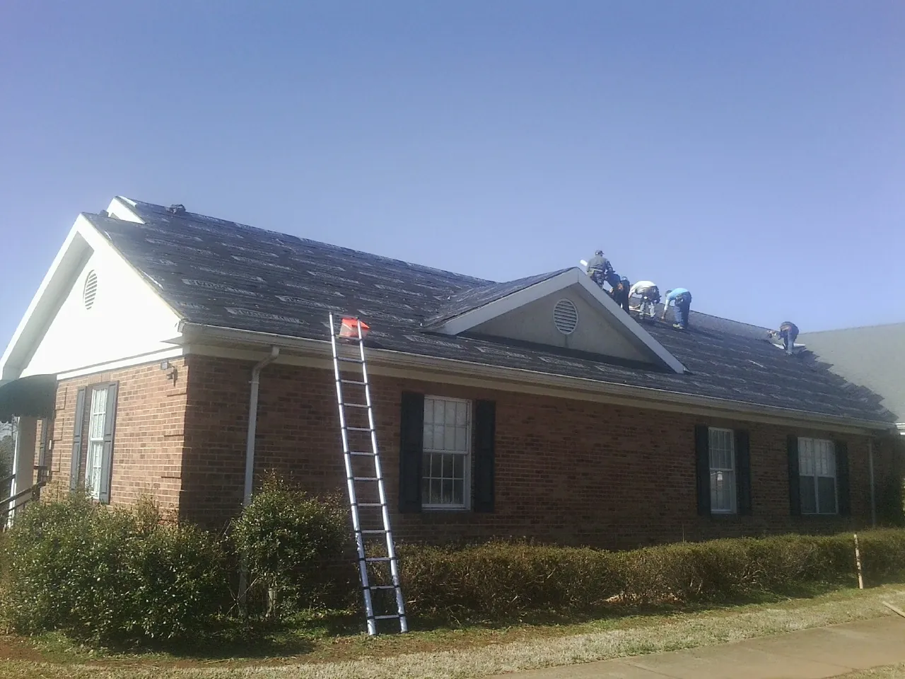 Crew tearing shingles off a brick ranch roof with a ladder set — Metal Roof Repair work by our crew in Willard