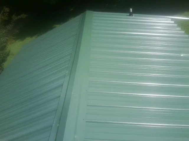 New green metal panels meeting at the ridge of a roof — Flat Roof Repair work by our crew in Willard